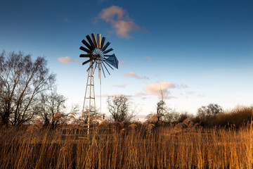Wind pump with blue sky and farmland in background.