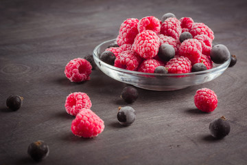 Frozen raspberries in a glass saucer. Frost on the berries. Dark background.