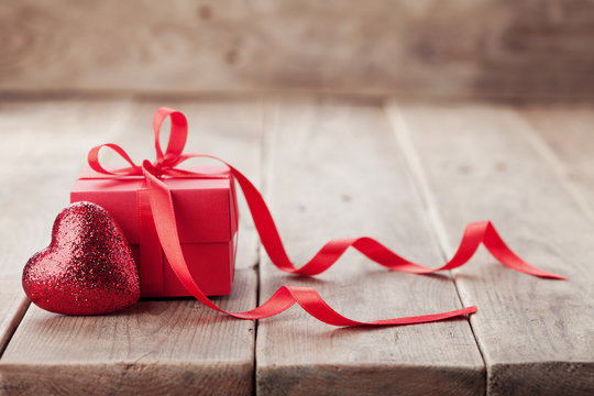 Gift or present box with red bow ribbon and glitter heart on rustic background for Valentines day.