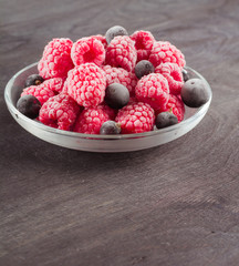Frozen raspberries in a glass saucer. Frost on the berries. Dark background.