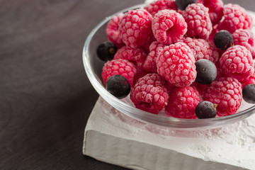 Frozen raspberries in a glass saucer. Frost on the berries. Dark background.