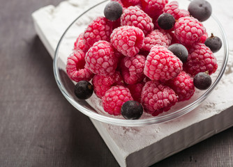 Frozen raspberries in a glass saucer. Frost on the berries. Dark background.