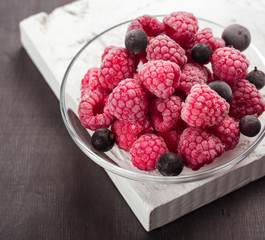 Frozen raspberries in a glass saucer. Frost on the berries. Dark background.