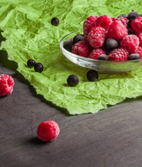 Frozen raspberries in a glass saucer. Frost on the berries. Dark and green background. Green crumpled paper.