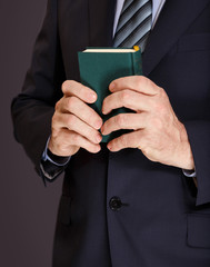 A man in a jacket holds in both hands a small book in the green cover