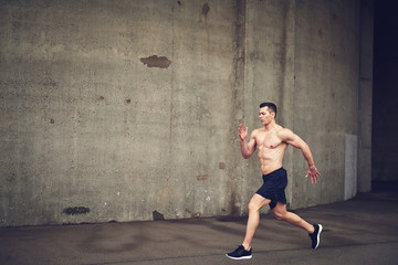 Shirtless young male running against concrete wall