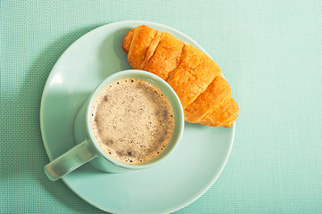 aquamarine mug with coffee and croissant from top angle
