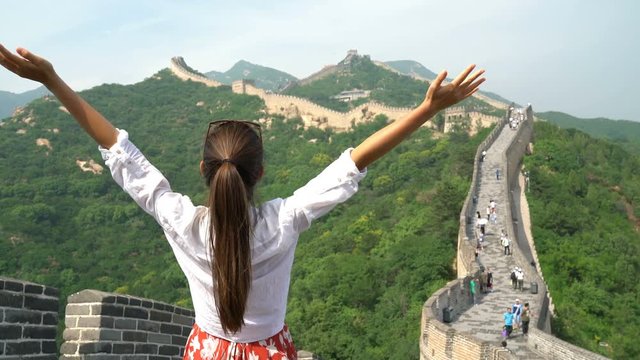 Happy cheerful tourist woman at Great Wall of China having fun free in freedom pose with arms up on travel during vacation trip in Asia. Girl visiting and sightseeing Chinese attraction in Badaling