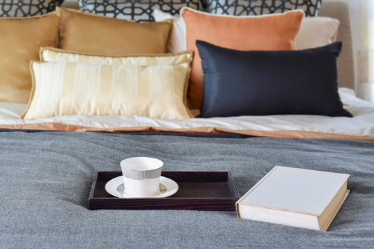 modern bedroom interior with teacup on decorative wooden tray and white book on the bed