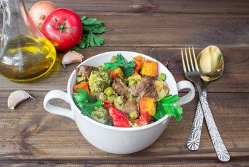 served beef meat stewed with vegetables in ceramic pot with ingredients on wooden background