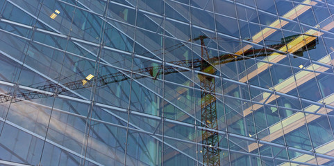 Visual illusion of constitution crane trapped inside the glass building. Reflection of construction crane in a modern glass building.