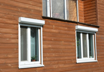 Windows with rolling shutter protection on the wooden house facade exterior