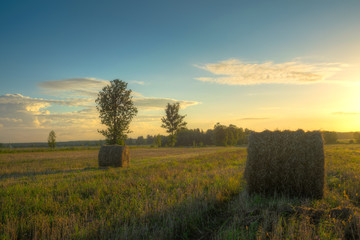 Sun just rises over a field of stubble with haystacks. August countryside landscape. HDR image..