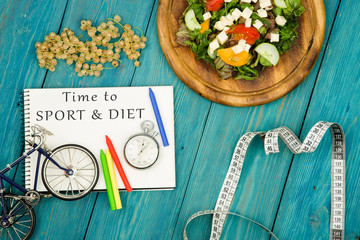 bicycle model, salad of fresh vegetables, notepad with text "Time to SPORT & DIET", stopwatch and tape measure