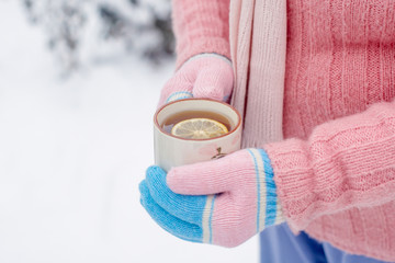 Woman in mittens holding a cup of tea with lemon in winter