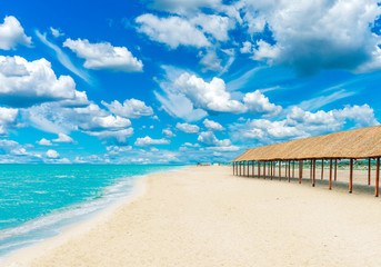 Beautiful tropical sandy beach with canopies from the sun and blue cloudy sky