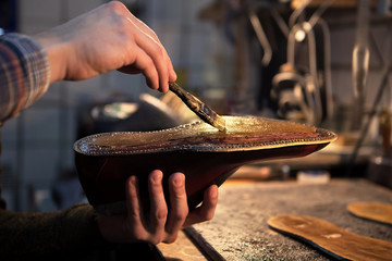 Shoemaker makes shoes for men. He smears special liquid  with a brush.