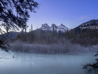 Sunrise view of the Three Sisters from a frozen Policemen's Creek along the Bow River outside Canmore, Alberta in winter.