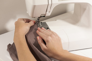 Hands sewing on white  machine brown fabric