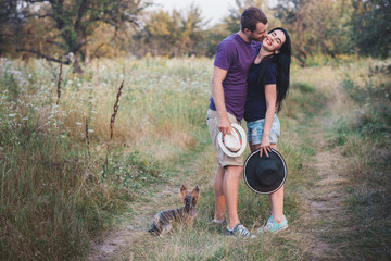 Fototapeta premium Young couple with little dog yorkshire terrier dressed t-shirt and hat embracing and have fun on the road,travel, vacation, holidays, vacation, love, life style