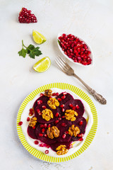 Dietary vegetarian salad of roasted beets with pomegranate seeds, walnuts caramelized in honey and natural yoghurt. Slices of lime, vintage fork, white and gray table, top view.