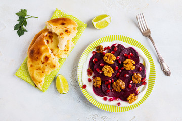 Dietary vegetarian salad of roasted beets with pomegranate seeds, walnuts caramelized in honey and natural yoghurt. Slices of lime, freshly baked bread, vintage fork, white and gray table, top view.