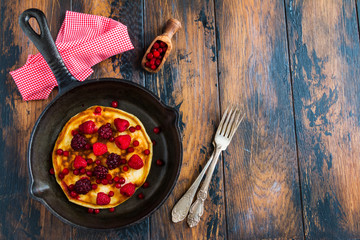 Homemade fried pancakes on a black cast iron skillet. Above are berries, raspberries, cranberries...