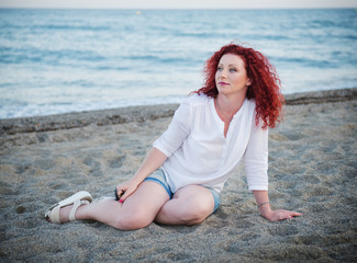 Fototapeta na wymiar Pretty red-haired girl sitting on the sand