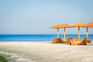 New wooden umbrellas, chair and sunbeds on the beach on a sunny day