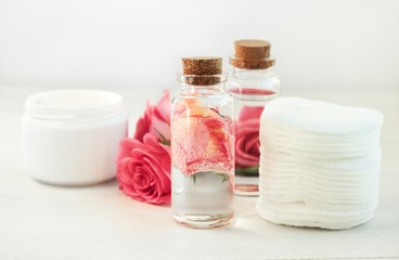 Facial lotion floral extract. Glass bottle with attar bubbles and rose petals, cotton pads. Healing homemade skincare moisture tonic. Gentle soft focus.