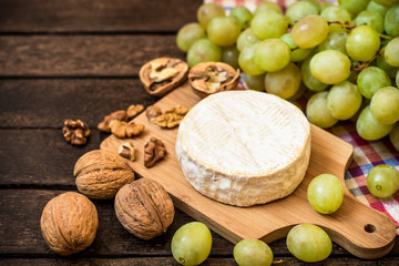 Camembert cheese with walnuts and green grapes on wooden rustic background