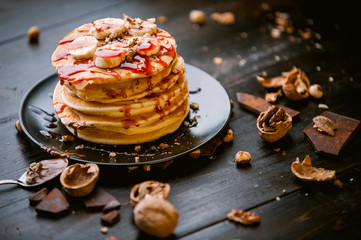 Pancake with chocolate and nut paste, walnuts and banana on a black plate