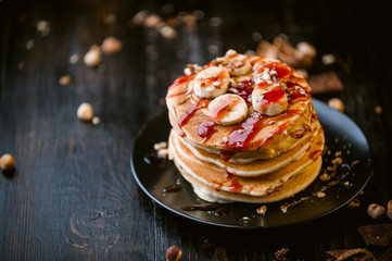 Pancake with chocolate and nut paste, walnuts and banana on a black plate