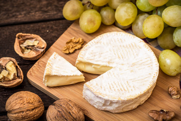 Camembert cheese with walnuts and green grapes on wooden rustic background
