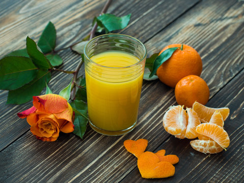 Fresh orange juice and beautiful rose on wooden table