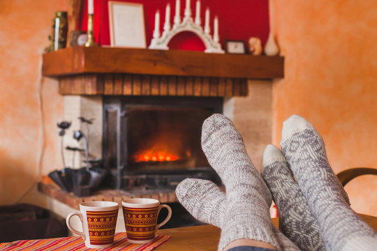 cozy family evening at home near fireplace in winter, feet of couple in socks and two cups of tea, weekend