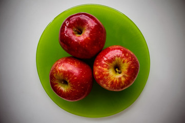 Three red apple on a green plate. The view from the top.