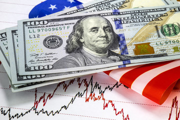 Stock market prices chart. Hundred us dollar bills above the graph. Black and red lines of prices on the chart. Us flag as background. Macro image
