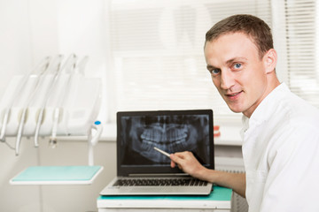 Fototapeta na wymiar Positive dentist showing on a laptop teeth x-ray picture in dental clinic office. stomatology and health care concept
