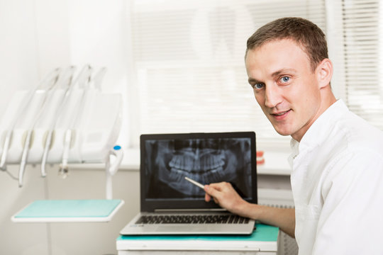 Positive dentist showing on a laptop teeth x-ray picture in dental clinic office. stomatology and health care concept