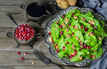 Fresh delicious salad with watercress,pomegranates and walnut served in vintage silver plate on rustic wooden background.Top view..