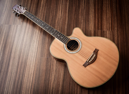 Acoustic guitar laid on wooden floor background.
