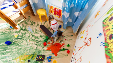 two children play paint brush colors on the wall in the room