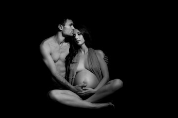 Naklejka premium Monochrome portrait of happy loving couple in a moment of love and tenderness. Pregnant woman with hands over tummy. Black and white photo.