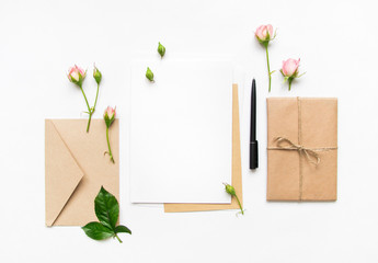 Letter, envelope and gift on white background. Invitation cards, or love letter with pink roses. Holiday concept, top view, flat lay