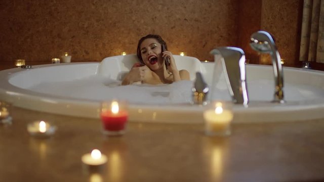 beautiful woman talking by cell phone and shaking a card sitting in the bath