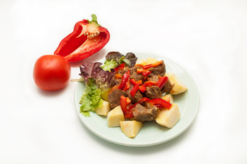 Hot dish of meat with vegetables and salad on a white background. View from above