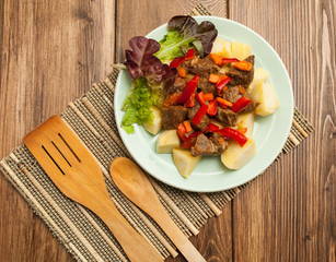 Hot dish of meat with vegetables and salad on a wooden background. View from above