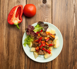 Hot dish of meat with vegetables and salad on a wooden background. View from above