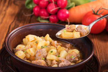 Stew with potatoes and meat in a ceramic plate on a wooden table.